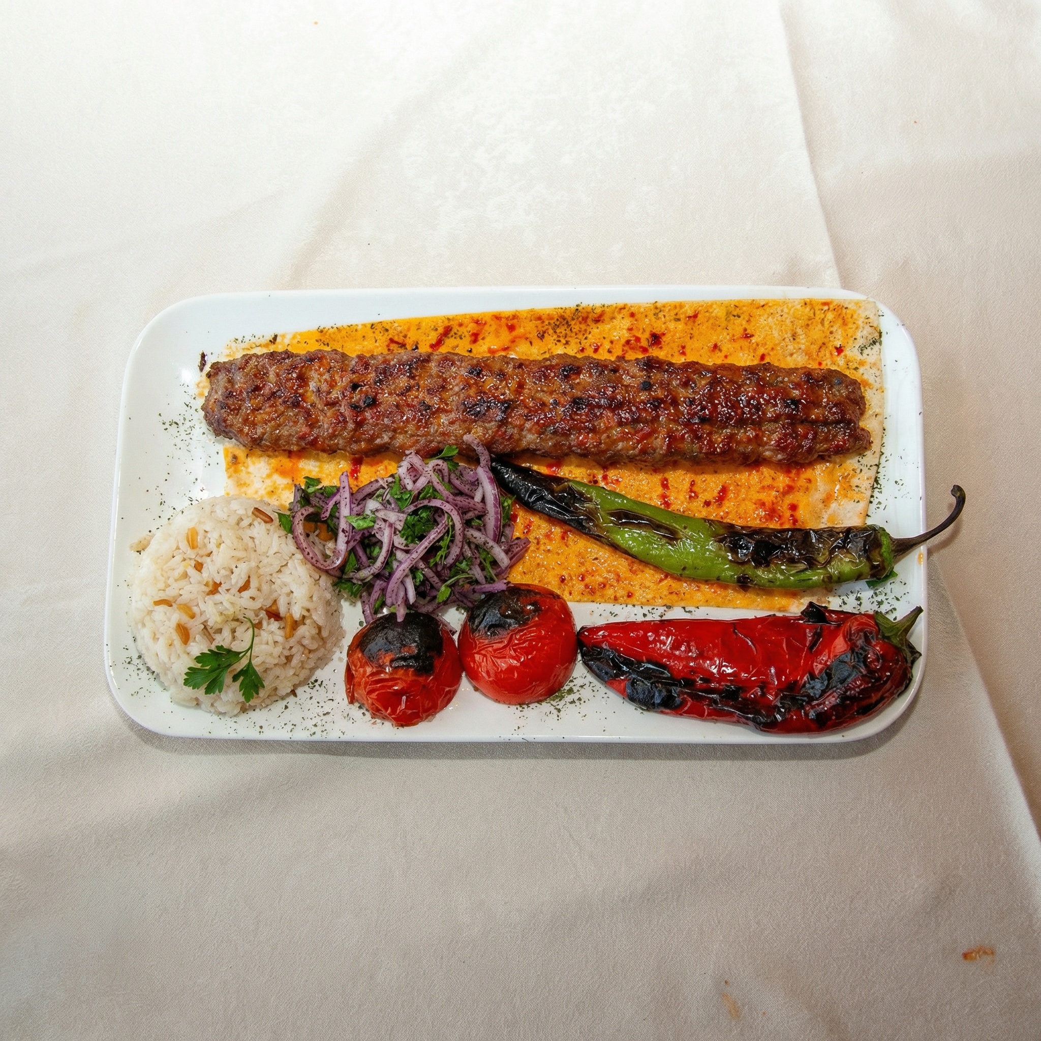 Traditioneller türkischer Adana Kebab auf Fladenbrot mit Reis und Grillgemüse.