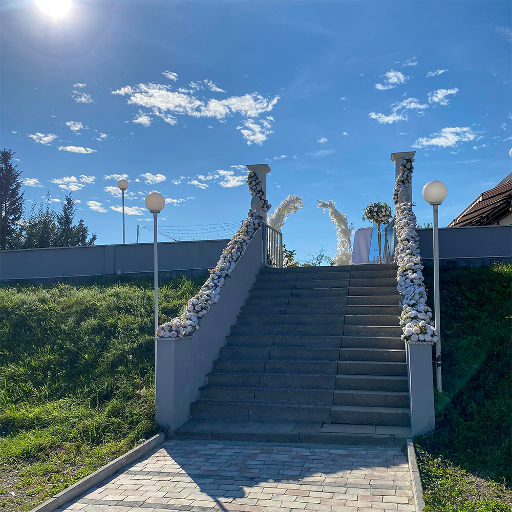 Festlich dekorierte Außentreppe mit weißen Blumenarrangements und Blumenbogen für eine türkische Hochzeit bei strahlendem Sonnenschein.