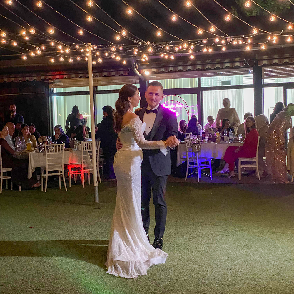 Brautpaar tanzt den Hochzeitstanz im Freien unter einer romantischen Lichterkette bei Nacht.