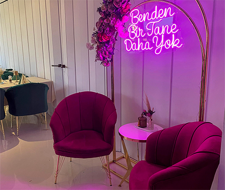 Pinke Samtsessel vor einem goldenen Bogen mit türkischer Neon-Aufschrift "Benden Bir Tane Daha Yok".